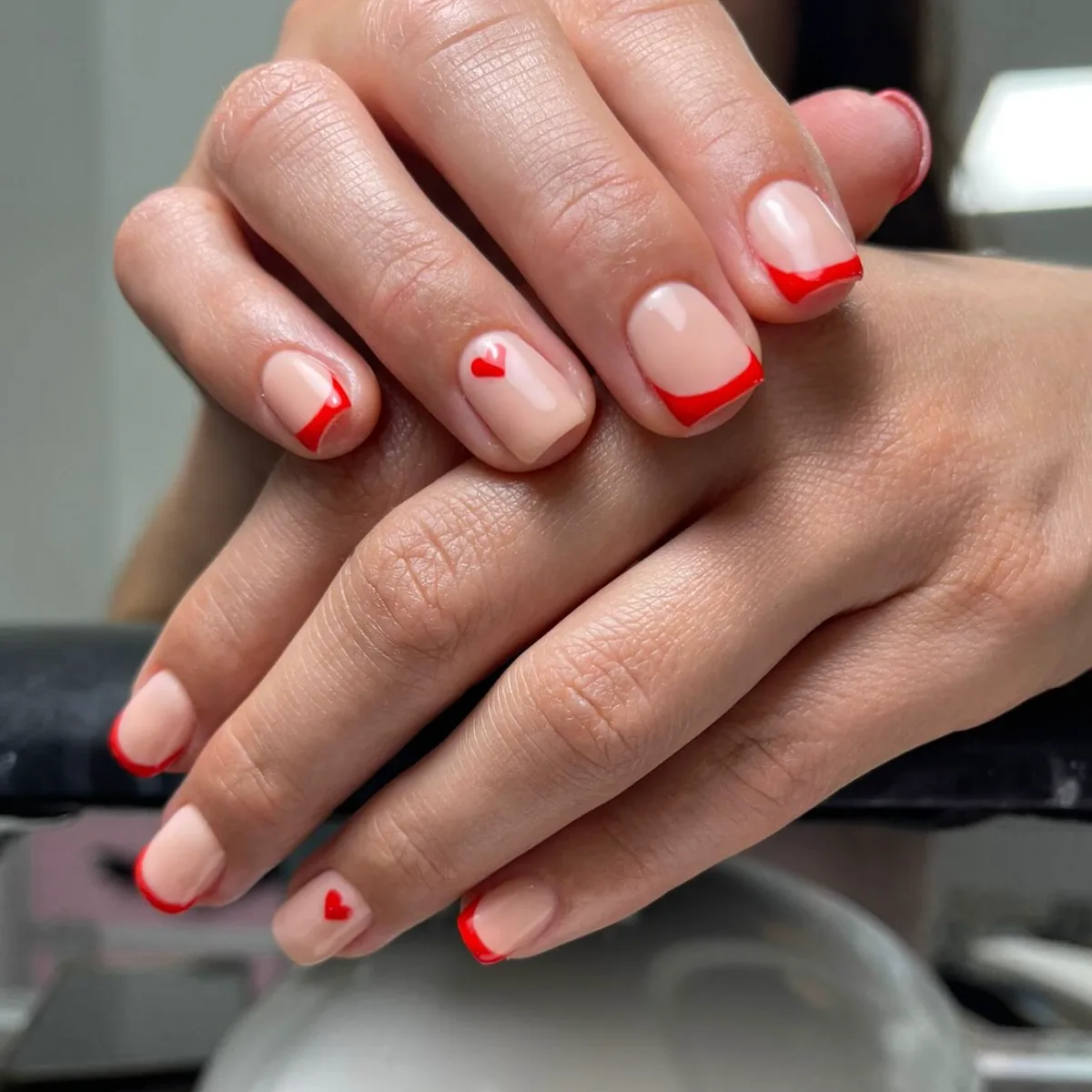Manicura nude con puntas rojas y pequeños corazones.