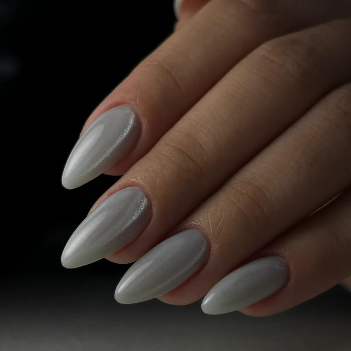 Uñas almendradas perladas sobre fondo oscuro.
